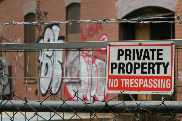 void-property-perimiter Generic void property image - a fence with "no trespassing" sign and a wall with graffiti in the background